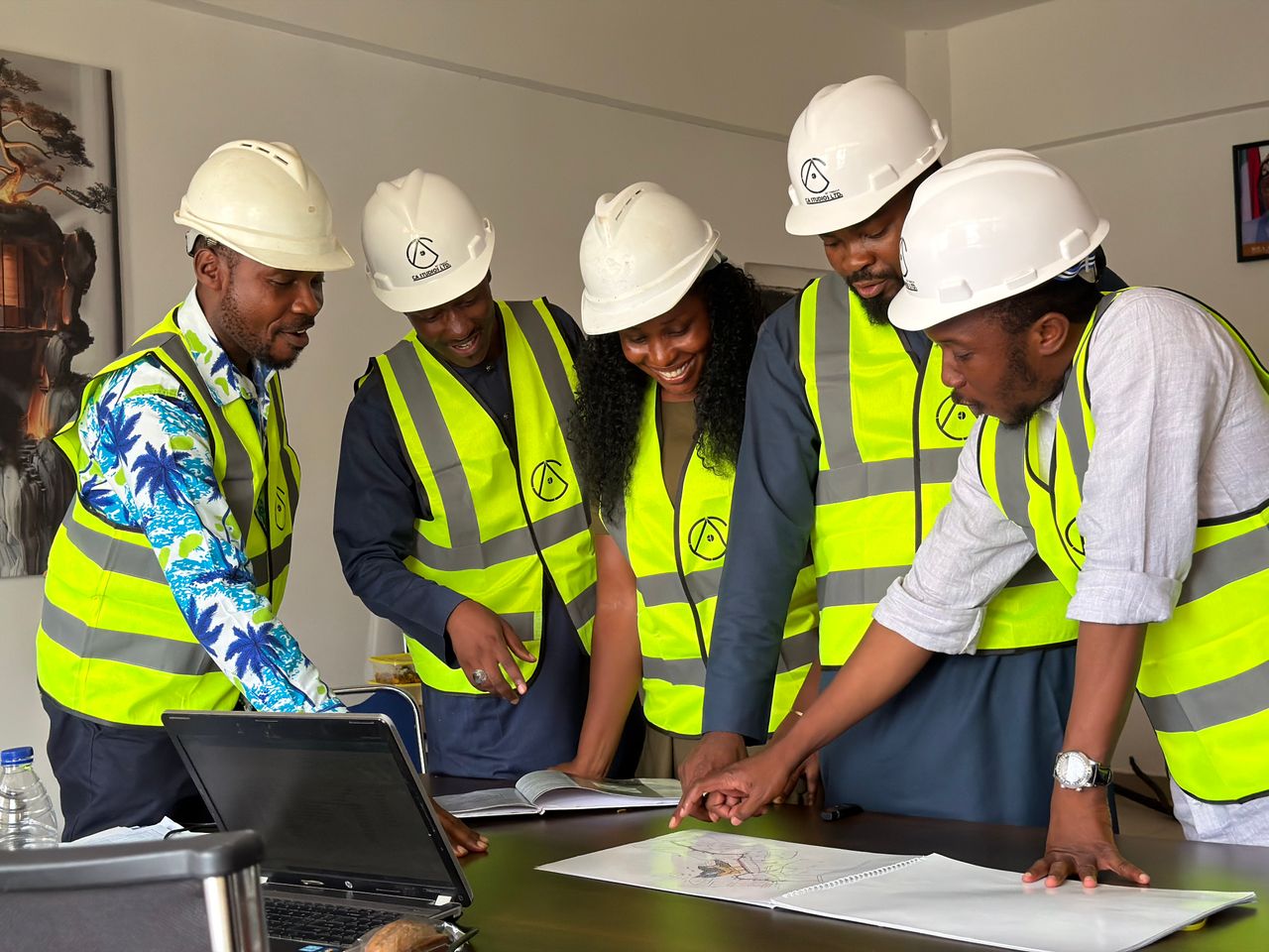 Group of engineers in hard hats and safety vests reviewing blueprints in an office setting.